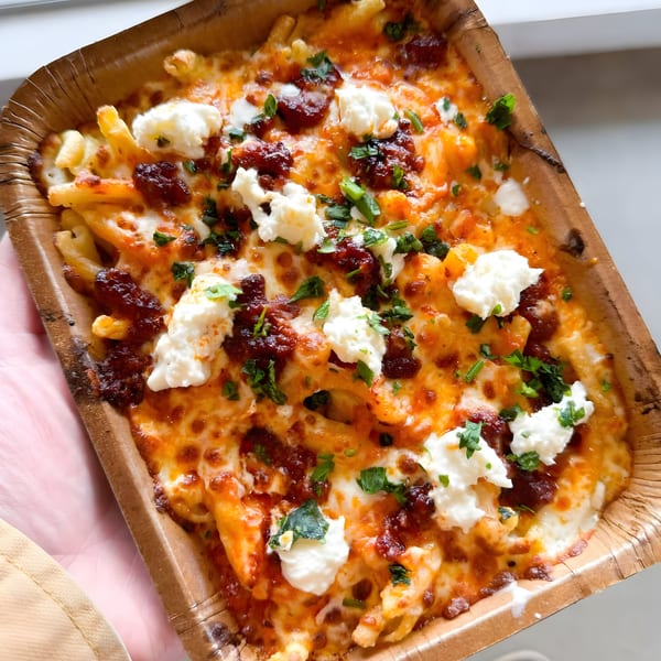 Porano's baked pasta with melted cheese, red sauce, ricotta, and fresh herbs in a brown container.